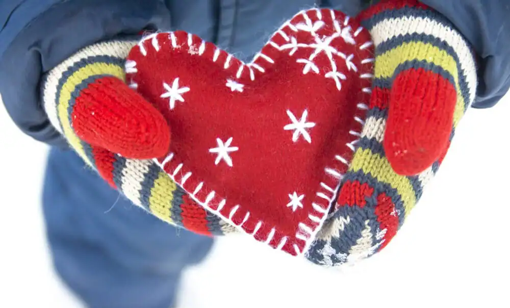 Person holding a red Christmas heart-shaped ornament with snowflake patterns.