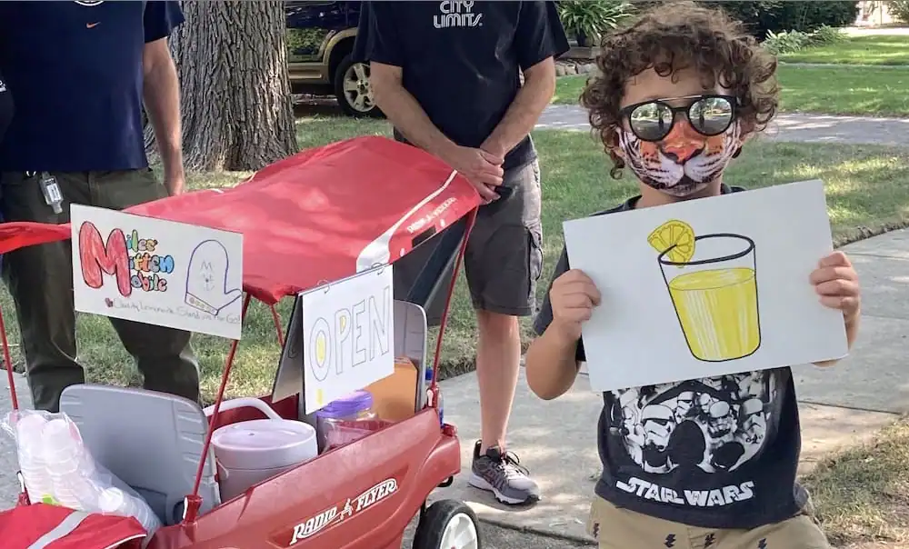 Child with curly hair and sunglasses holding a lemonade drawing at MFD Staging.